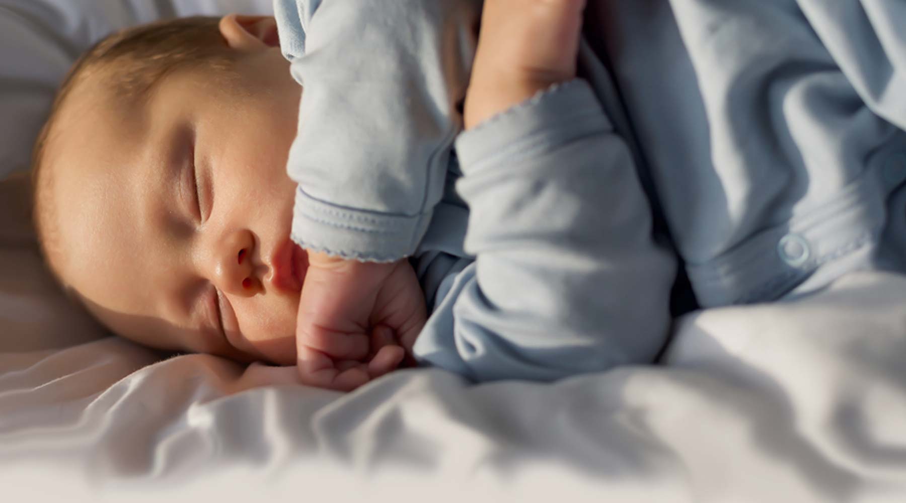 Bebis som ligger på sidan och sover, iklädd en gråblå sovpåse i ekologisk bomull