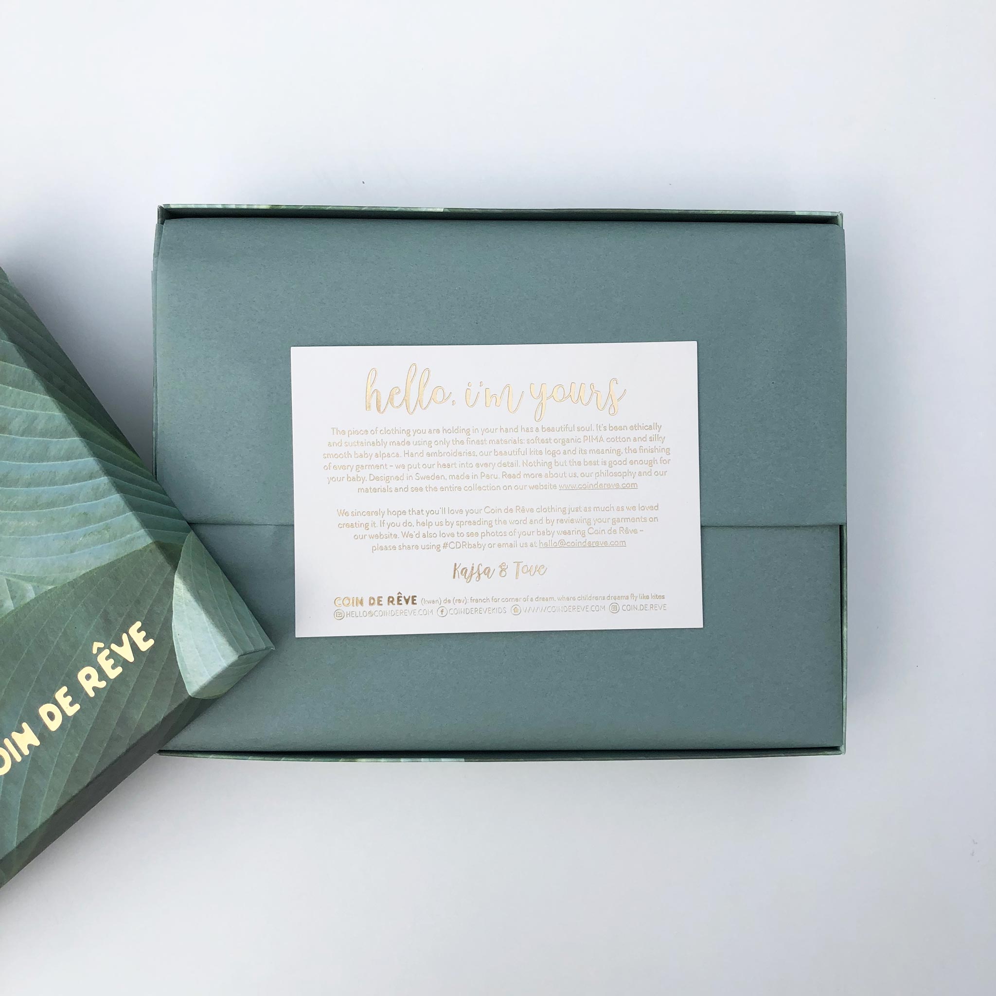 Presentlåda och silkespapper i Dusty Green med guldpräglat kort med information om varumärket Coin de Rêve