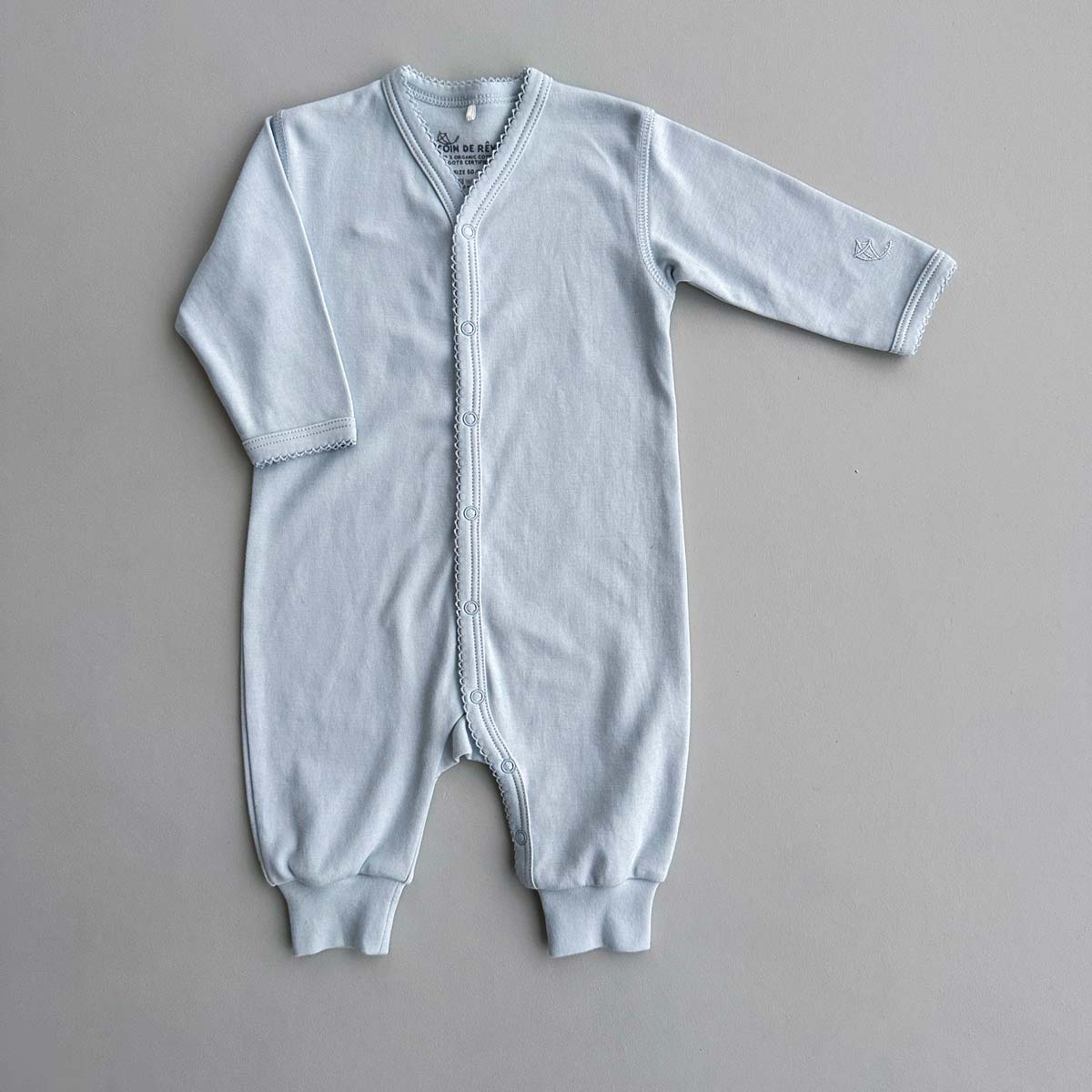 Ljusblå jumpsuit i ekologisk bomull med spetskant på flat bakgrund