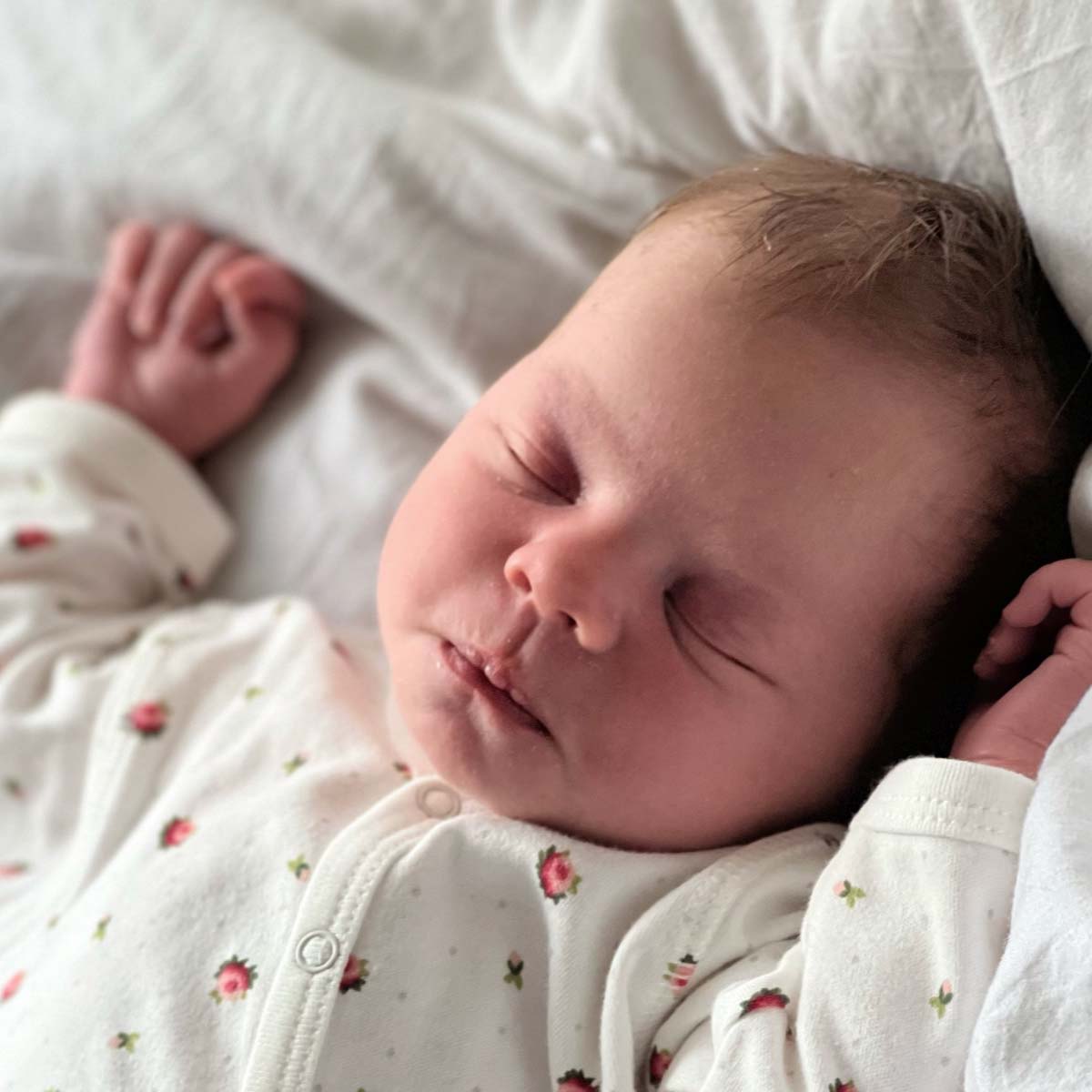 Närbild på svande bebis i jumpsuit i ekologisk och GOTS-certifierad bomull med blommigt print