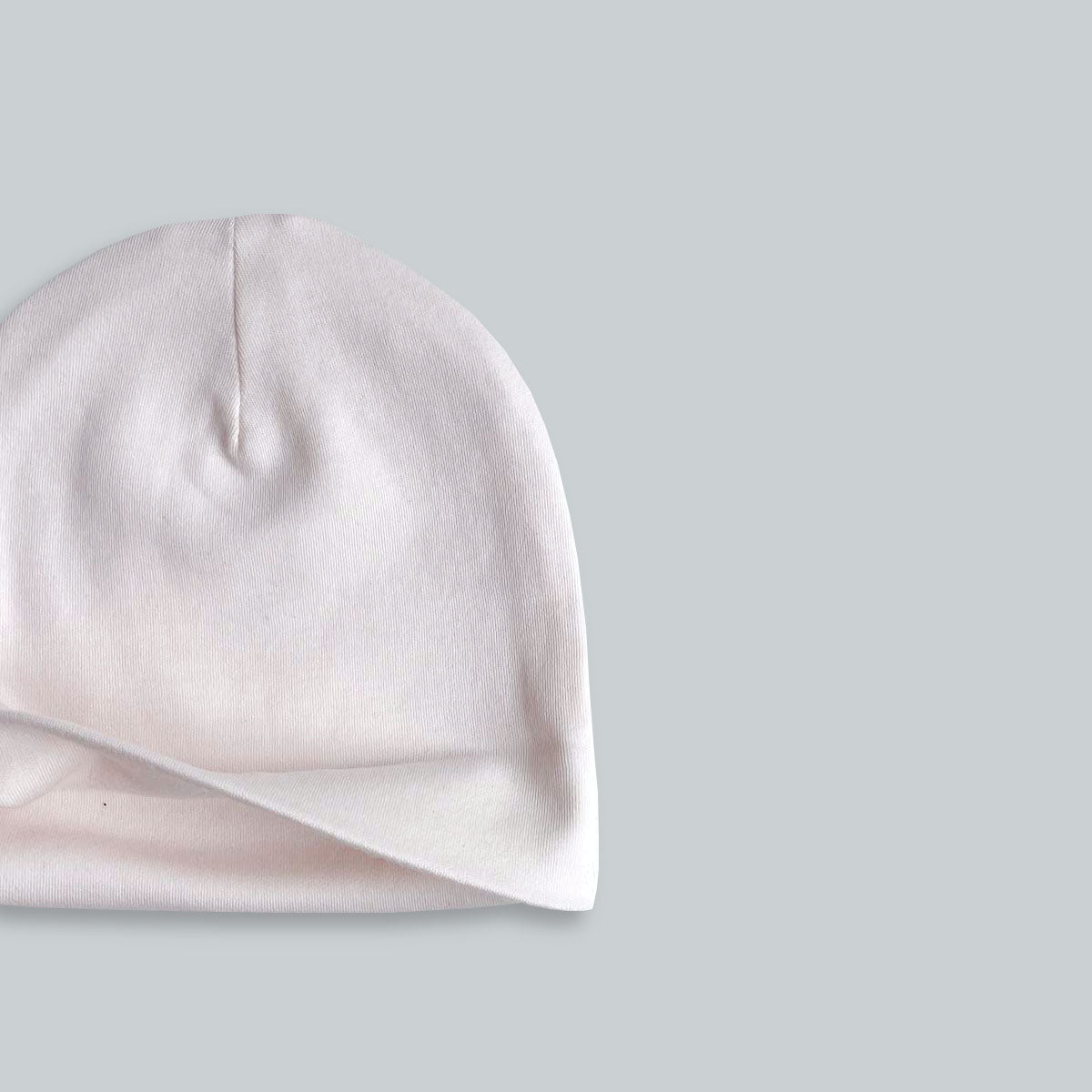 Detalj från krämrosa mössa för baby i mjuk ekologisk pimabomull