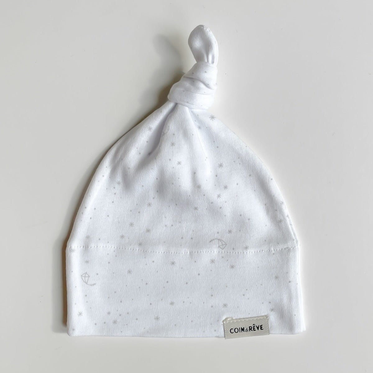 Nedvikt vit babymössa med knut i 100% ekologisk bomull. Grått print med drakar och stjärnor.