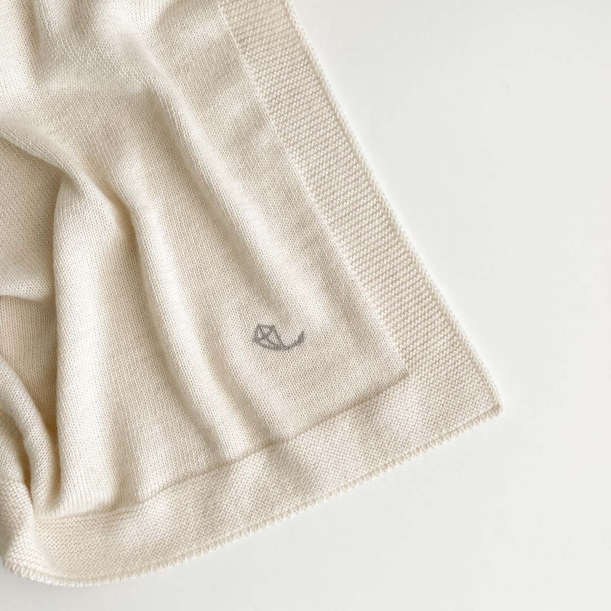 Detalj från krämvit stickad babyfilt i premium alpaca-ull med broderad logo