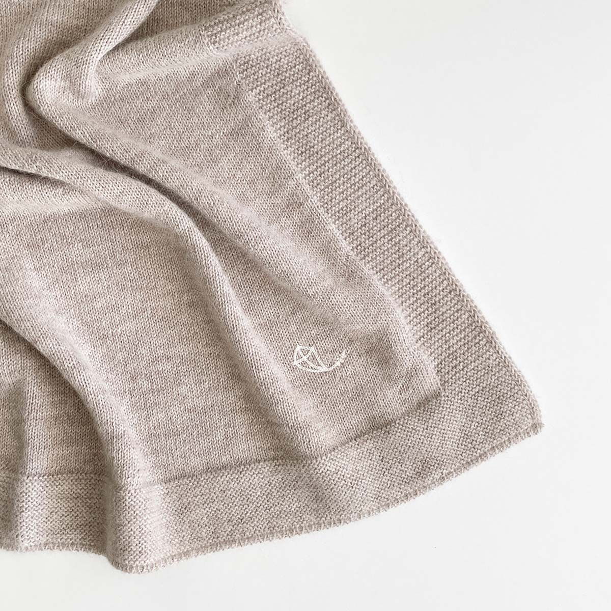 Detalj från beige stickad babyfilt i premium alpaca-ull med broderad logo