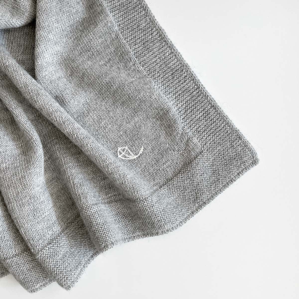 Detalj från grå stickad babyfilt i premium alpaca-ull med broderad logo