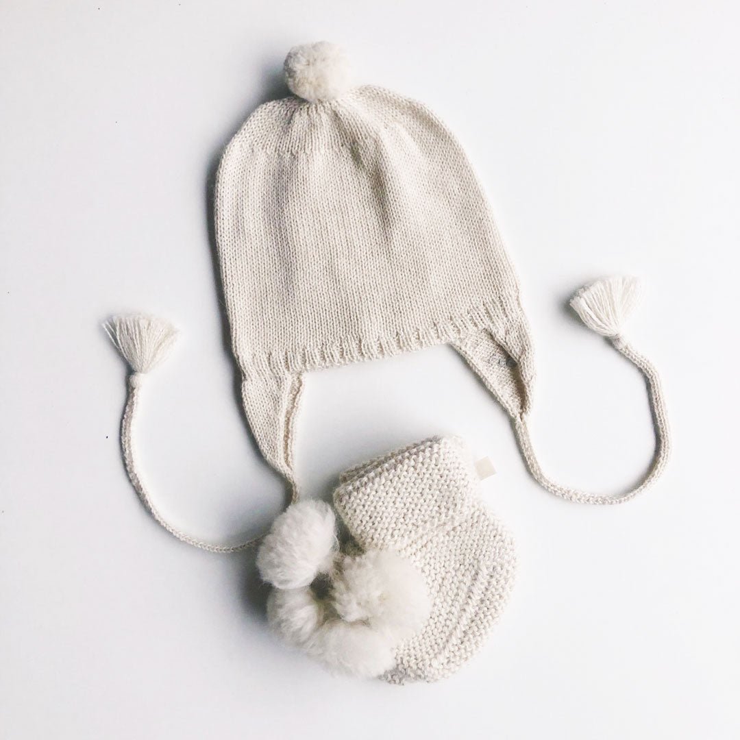 Vit stickad bebismössa i ekologisk pimabomull med pompom och öronlappar samt stickade tossor med tofs