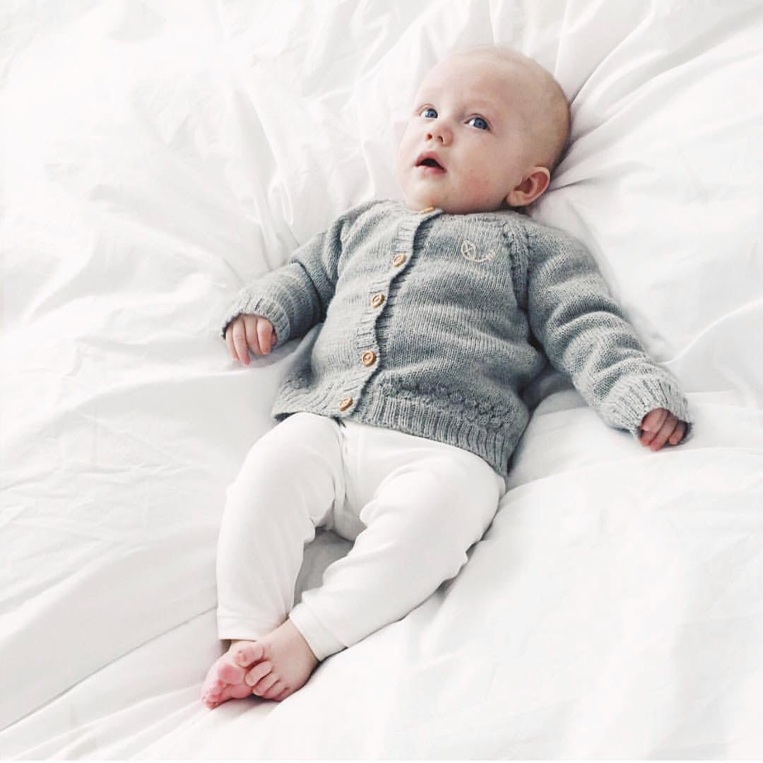Bebis som ligger på ett vitt täcke iklädd leggings i Milky White och Anholt Baby Cardigan i Smooth Grey