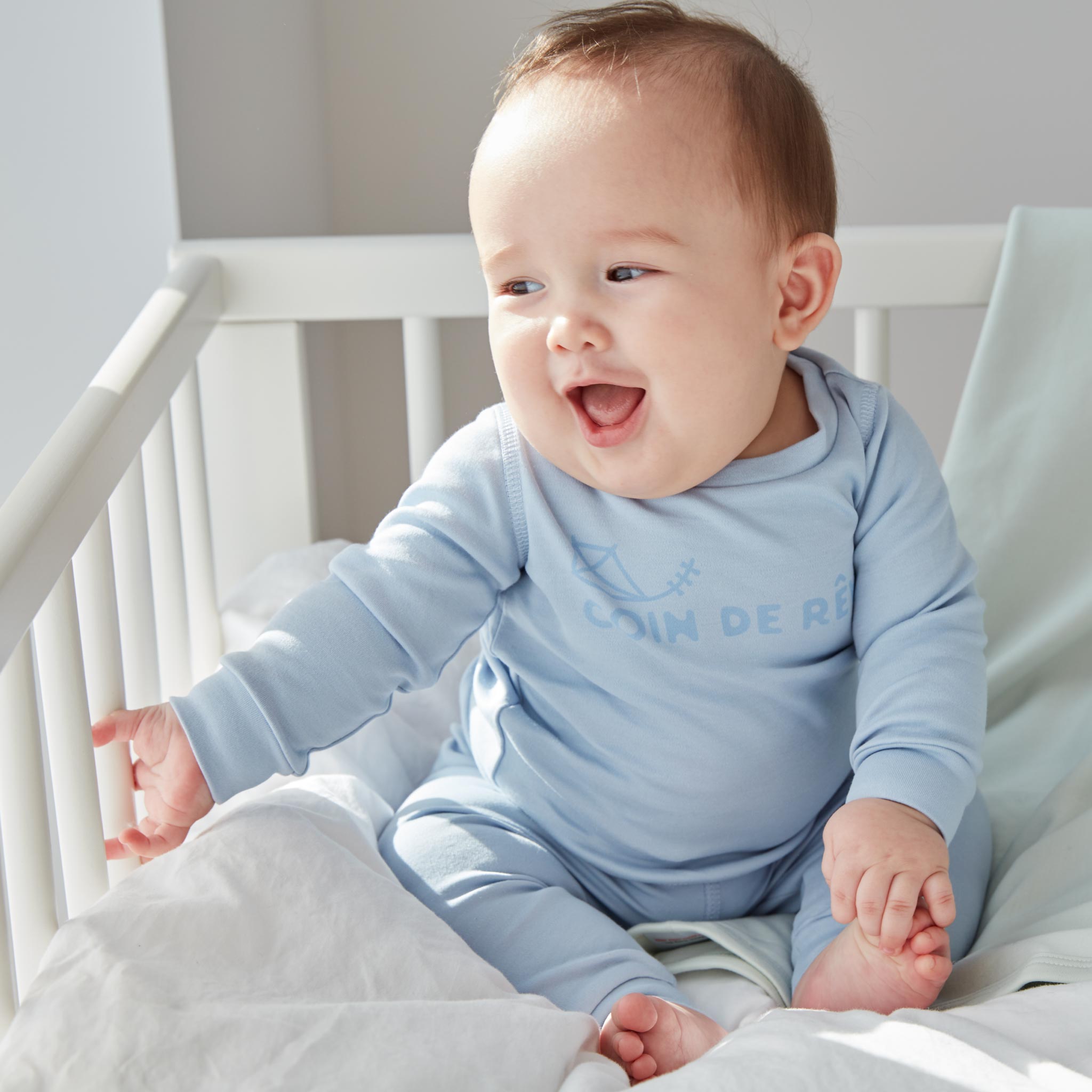 Söt bebis skrattar i tvådelad blå pyjamas i ekologisk bomull