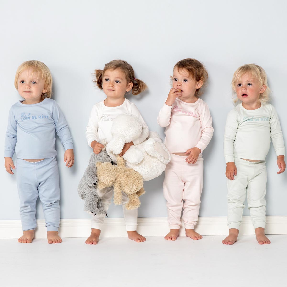 Barn som står mot en vägg iklädda pyjamasar i fyra olika färger i mjuk ekologhisk pimabomull