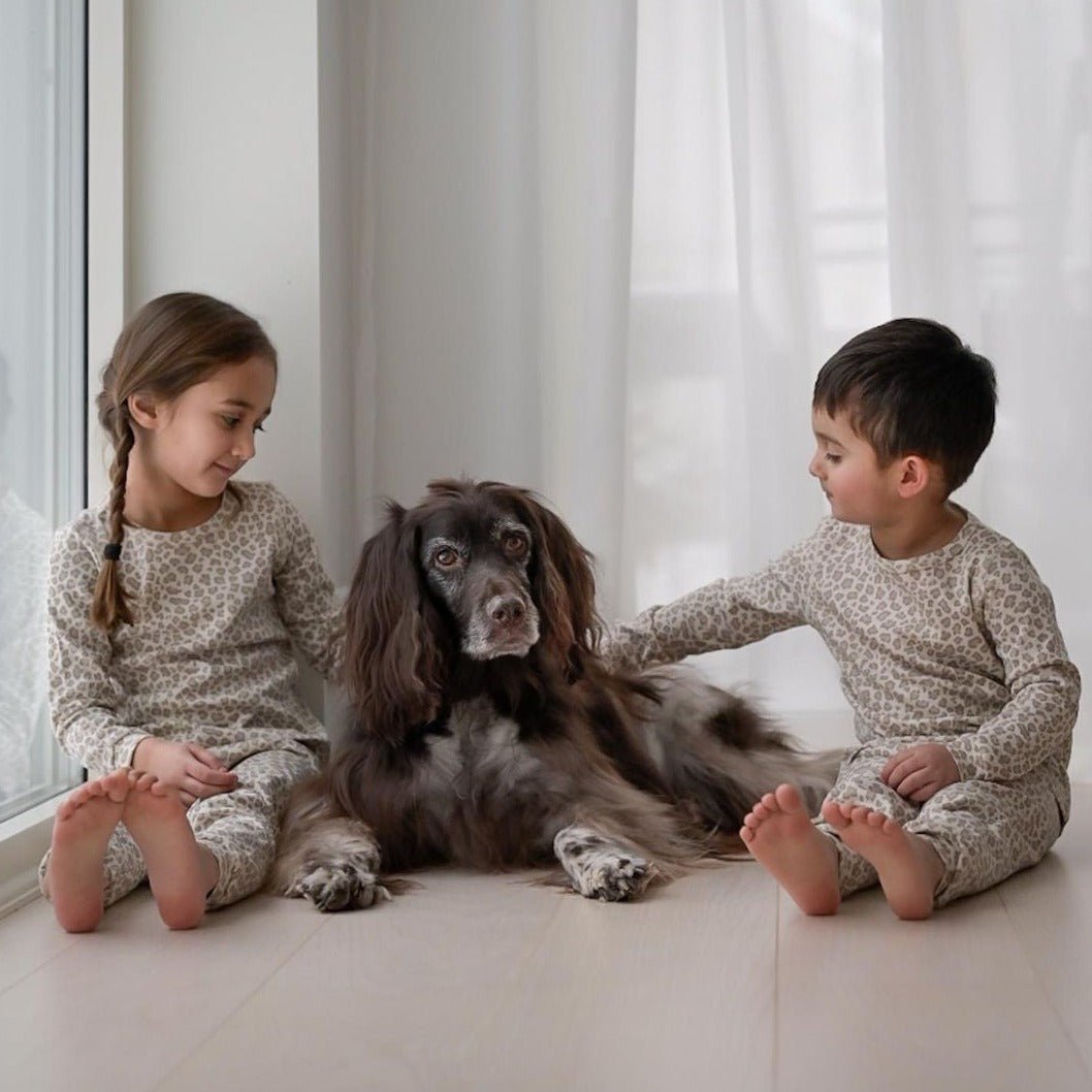 Två barn som kelar med en brun hund, iklädda långärmade pyjamasar i leopardprint