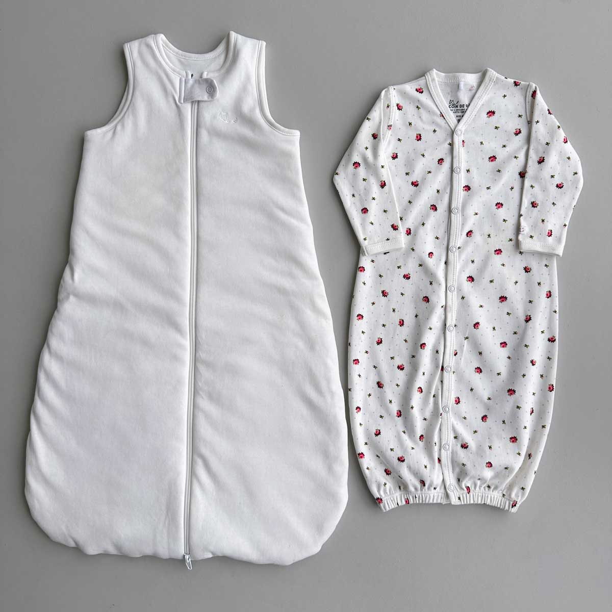 Krämvit Sovpåse (sleep sack) och blommig sovpåse (sleeping gown) bredvid varandra på plan grå yta.
