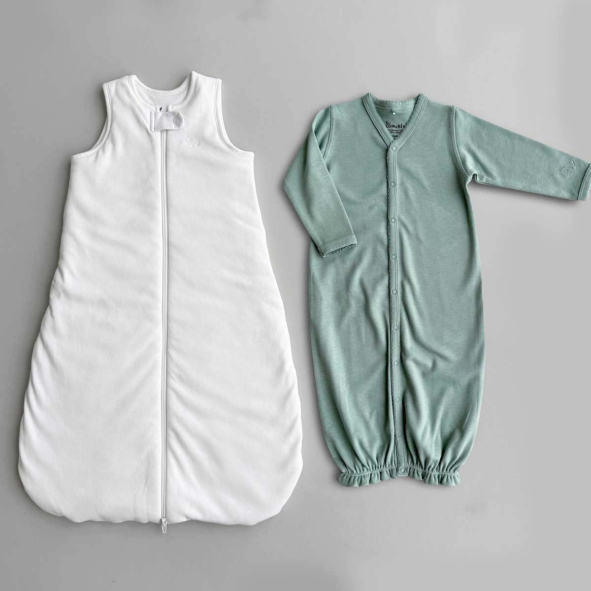 Krämvit Sovpåse (sleep sack) och grön sovpåse (sleeping gown) bredvid varandra på plan grå yta.