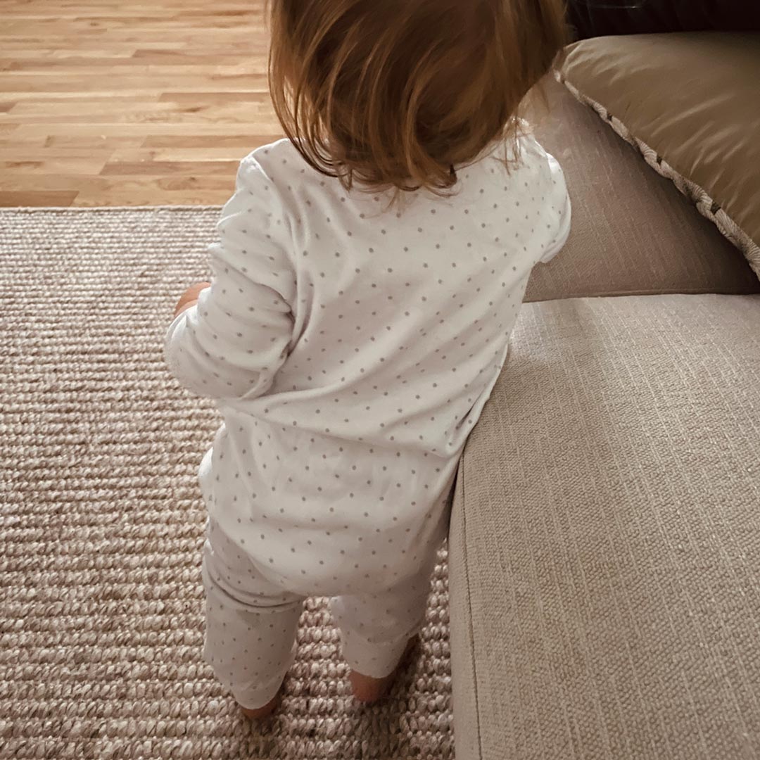 Bebis som står i vit onesie med grå prickar 